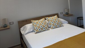 Un lit bien fait, agrémenté d’oreillers à motifs, une lampe de chevet et une petite étagère avec une lampe et un objet décoratif.