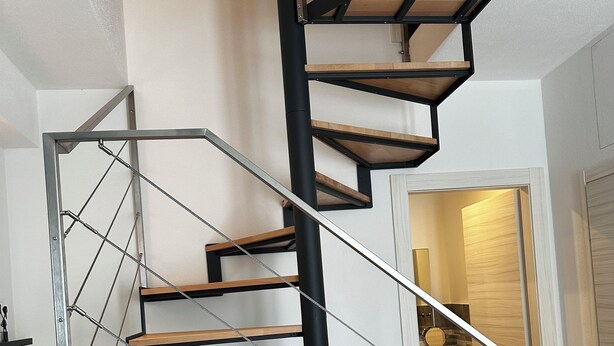 Un escalier en colimaçon moderne, avec des marches en bois et des rampes en métal, menant à l’étage supérieur.
