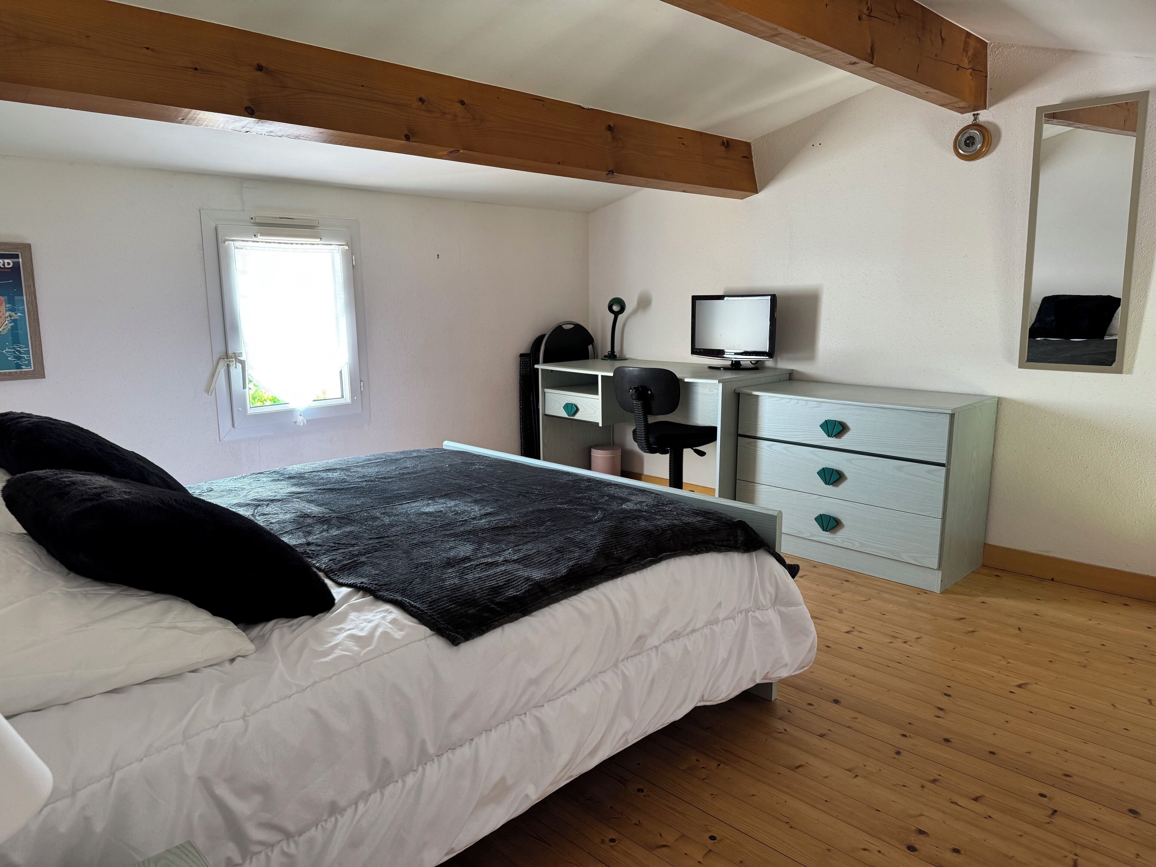 Quarto com cama, escrivaninha com computador, cadeira e janela.