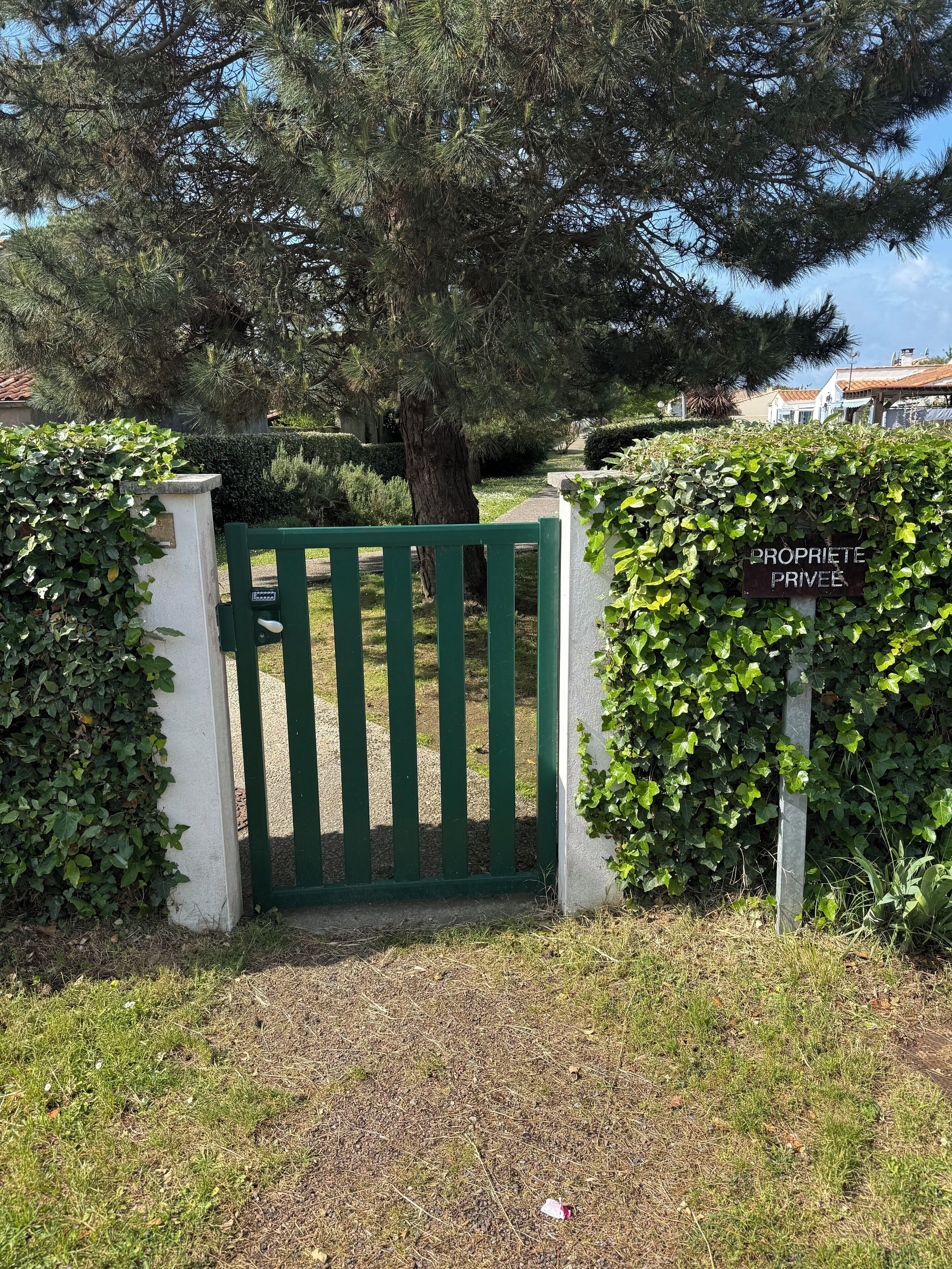 A gated entrance with a green gate, a hedge, and a sign that reads "PROPRIETE PRIVEE".