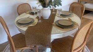 Une table de salle à manger ronde, agrémentée d’un vase blanc servant de centre de table, et entourée de quatre chaises en osier.