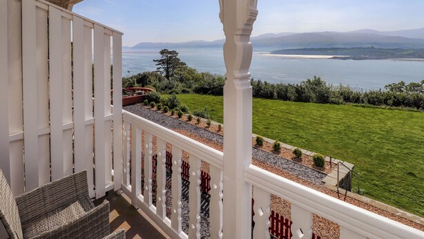 A balcony with a white railing, a view of a grassy area, and a body of water in the distance. - Menai View (Menai Bridge)
