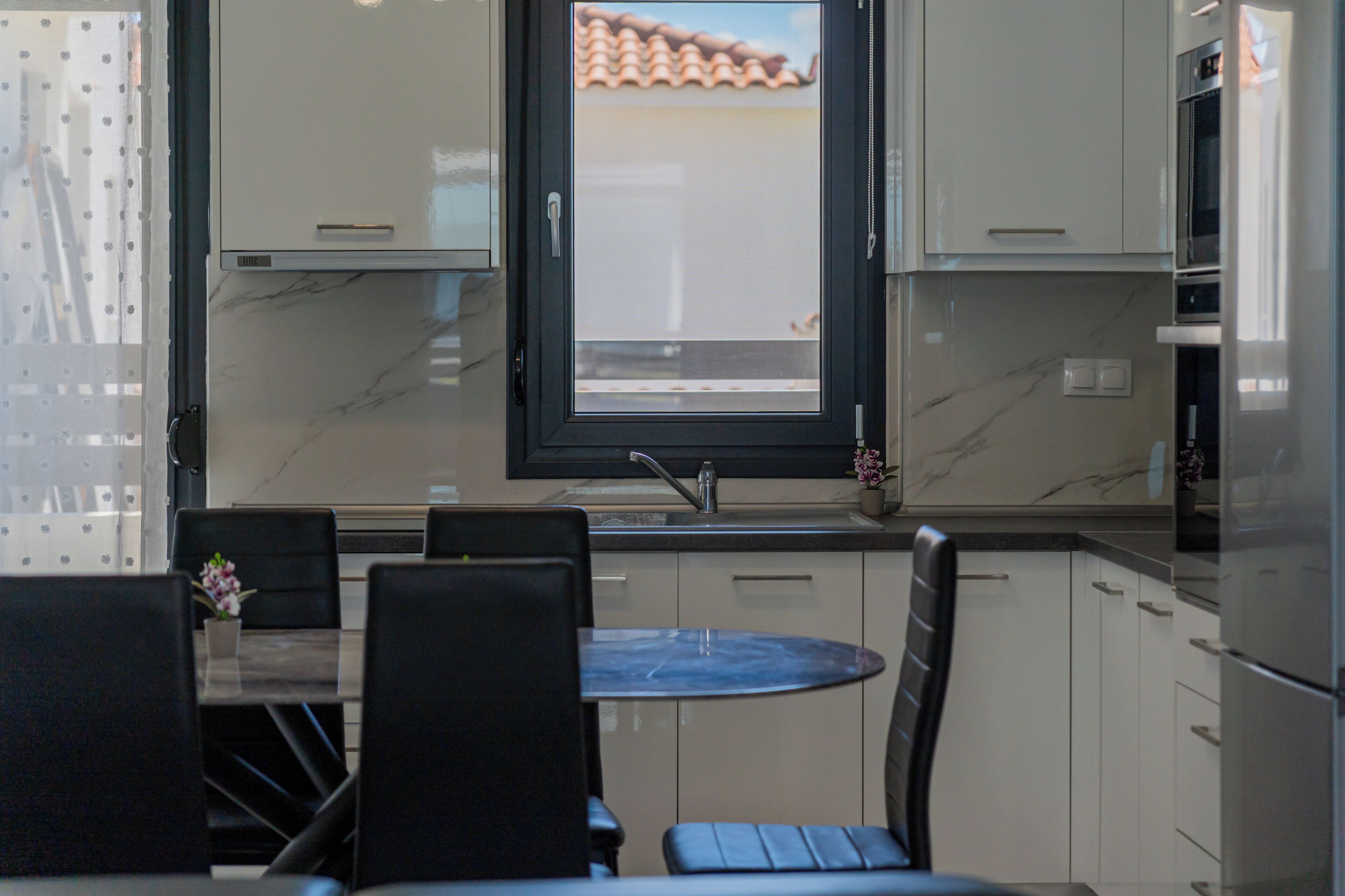 Eine moderne Küche mit Einbauofen, einem Fenster mit Blick auf das Dach und einem Essbereich mit Tisch und Stühlen.