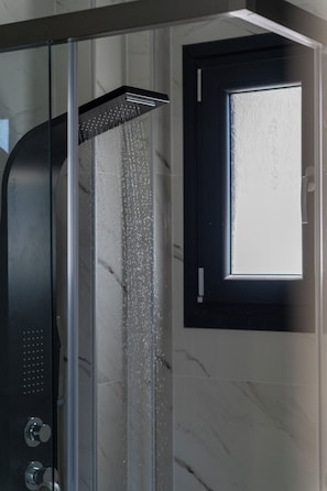 A shower with water running, a glass door, and a window with frosted glass.