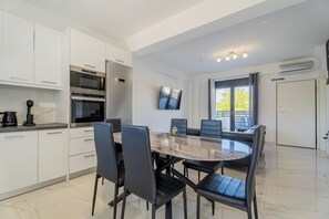 Une cuisine moderne avec des meubles blancs, un four encastré et un coin repas comprenant une table en marbre et des chaises noires.