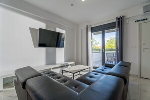 A modern living room with a sofa, a flat-screen TV, a coffee table, and a sliding glass door leading to an outdoor area.