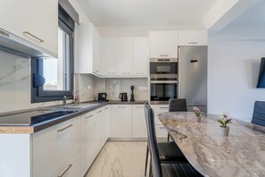 A modern kitchen with white cabinets, a marble countertop, a built-in oven, and a coffee machine.