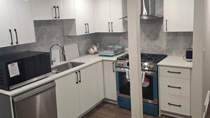 A modern kitchen with white cabinets, stainless steel appliances, and a wooden floor. - Cozy 2-Bedroom Suite: 5 Minutes Walk To Chestermere Lake (Chestermere)