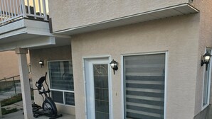 A residential building with a covered patio, a door with a glass panel, and a window with a closed shutter. - Cozy 2-Bedroom Suite: 5 Minutes Walk To Chestermere Lake (Chestermere)