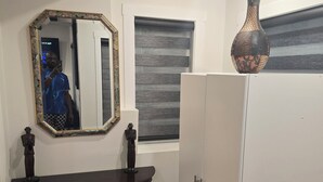 A room with a dark wooden console table, a white wardrobe, a decorative vase, and a mirror with a floral frame. - Cozy 2-Bedroom Suite: 5 Minutes Walk To Chestermere Lake (Chestermere)