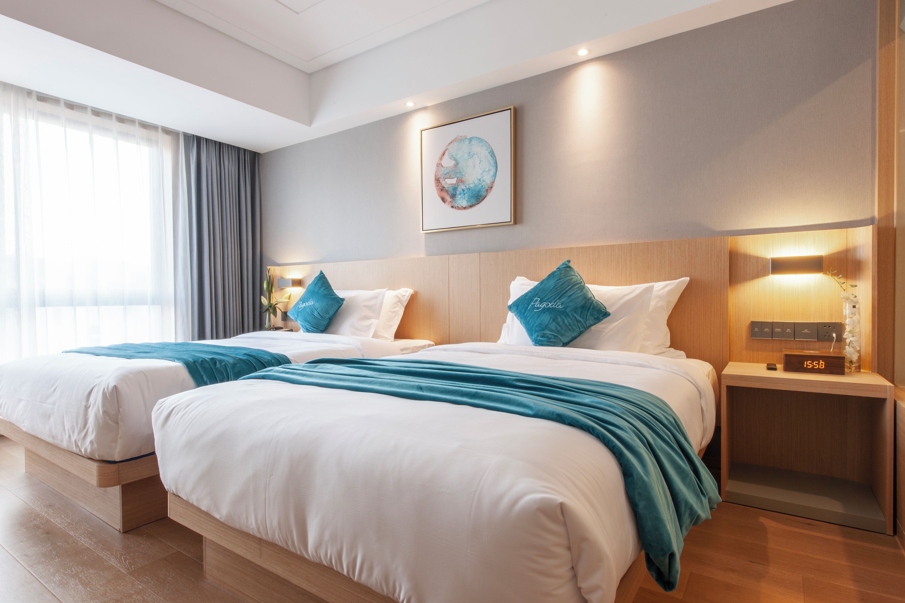 A hotel room with two beds, a bedside table with a clock, and a wall-mounted artwork.