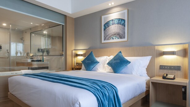 A modern hotel room with a large bed, a bedside table with a phone, a nightstand, a mirror, and a wall-mounted artwork. - Pagoda Hotel Shanghai Baixia near Jingan Temple (Shanghai)