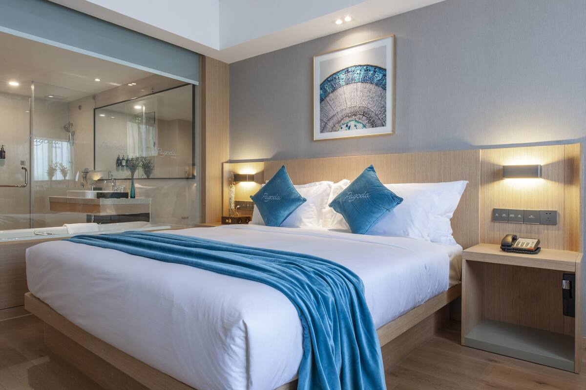 Una habitación de hotel moderna con una cama grande, una mesita de noche con un teléfono, un velador, un espejo y una obra de arte colgada en la pared.