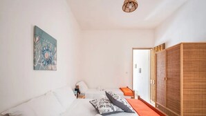 Un dormitorio con cama, almohadas, una toalla enrollada, una mesita de noche, una lámpara, un cuadro y un armario.
