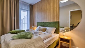 A neatly made bed with pillows and a blanket, a bedside table with a lamp, and a window with curtains. - Apartamenty Sun & Snow Belle View (Szklarska Poreba)