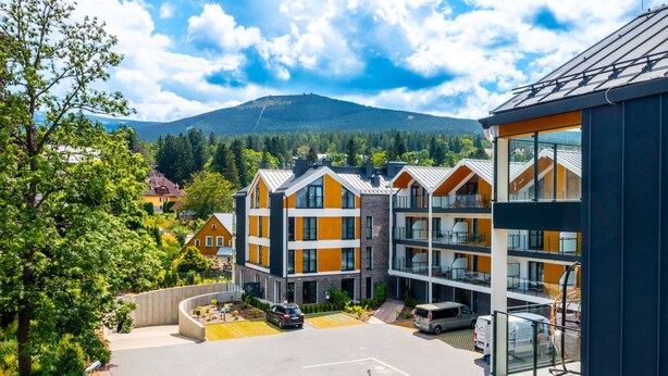 A modern multi-story building with a parking area, surrounded by greenery and mountains in the background. - Apartamenty Sun & Snow Belle View (Szklarska Poreba)