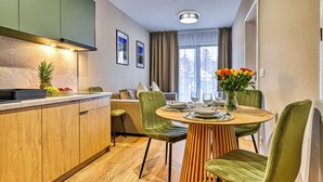 A modern kitchen with wooden cabinets, a dining area with a round table and green chairs, and a large window with curtains. - Apartamenty Sun & Snow Belle View (Szklarska Poreba)