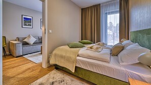 A modern hotel room with a bed, a sofa, a small table, and a view of the outdoors. - Apartamenty Sun & Snow Belle View (Szklarska Poreba)