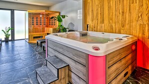 A modern spa room with a large hot tub, wooden paneling, and a seating area with a plant. - Apartamenty Sun & Snow Belle View (Szklarska Poreba)