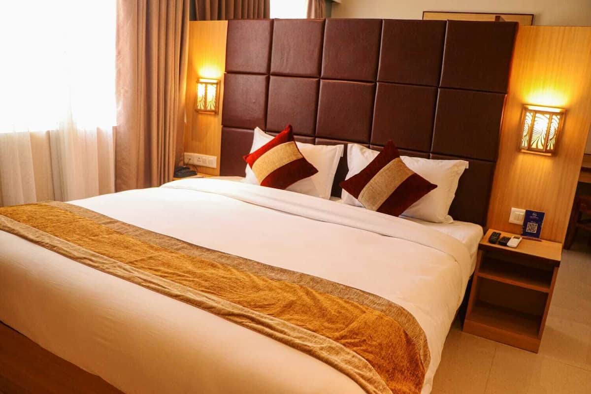 Una camera d'albergo con un letto grande, una testiera imbottita, due abat-jour e un comodino con un telecomando.