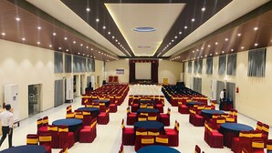 Un salón de conferencias amplio con filas de mesas y sillas, un escenario y cortinas.