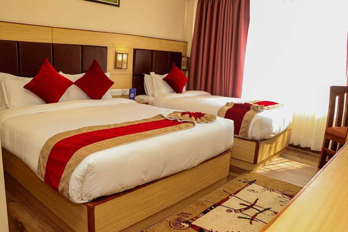 Una camera d'albergo con due letti, ognuno con biancheria rossa e bianca, una testiera in legno, un comodino e una tenda rossa.
