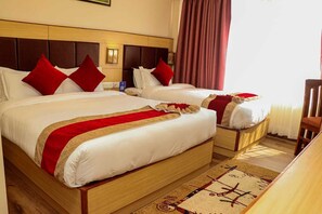 Habitación de hotel con dos camas, cada una con ropa de cama roja y blanca, cabeceros de madera, mesitas de noche y cortinas rojas.