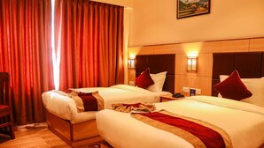 Habitación de hotel con dos camas, cabeceros de madera, cortinas rojas y un cuadro en la pared.