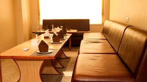 Una sala de conferencias con una larga mesa dispuesta para una reunión, un sofá de cuero y un ventanal que proporciona luz natural.
