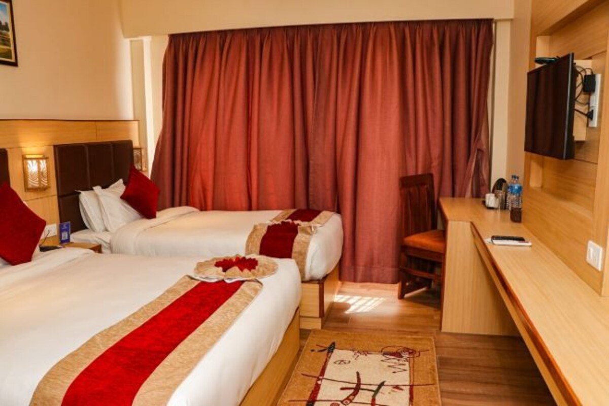 A hotel room with two beds, a desk, a chair, a TV, and a window with curtains.