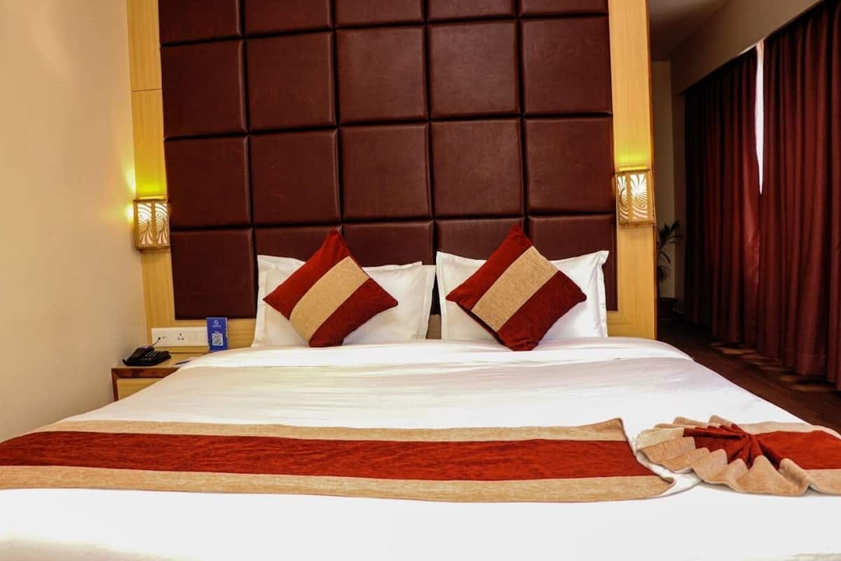 Camera d'albergo con un letto grande, una testiera imbottita, due abat-jour e una coperta beige e rossa.