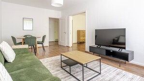 Un salon moderne avec un canapé vert, une table basse en bois, un téléviseur posé sur un meuble noir et un coin repas comprenant une table et des chaises.