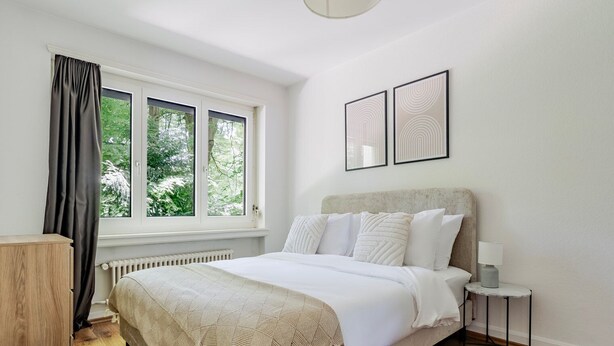 Une chambre à coucher avec un lit, une table de chevet, une lampe et une fenêtre avec des rideaux.