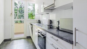 Une cuisine moderne avec des meubles blancs, un plan de travail noir et une vue sur la verdure à l’extérieur.