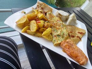 A plate of food including a fish fillet, potato wedges, and a rolled omelette, served on a white plate.