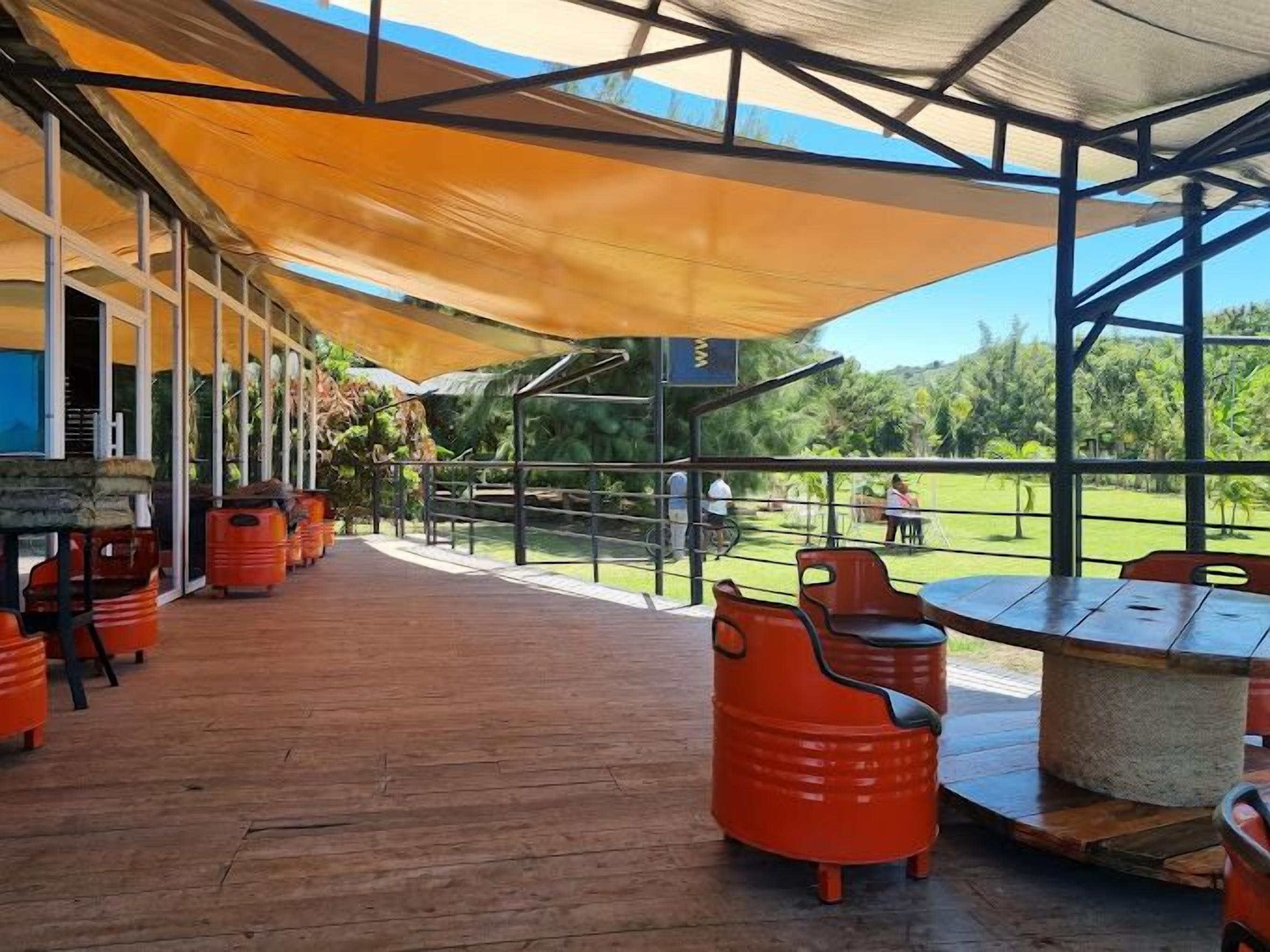 Patio esterno con pavimento in legno e sedie arancioni, affacciato su una zona verde.