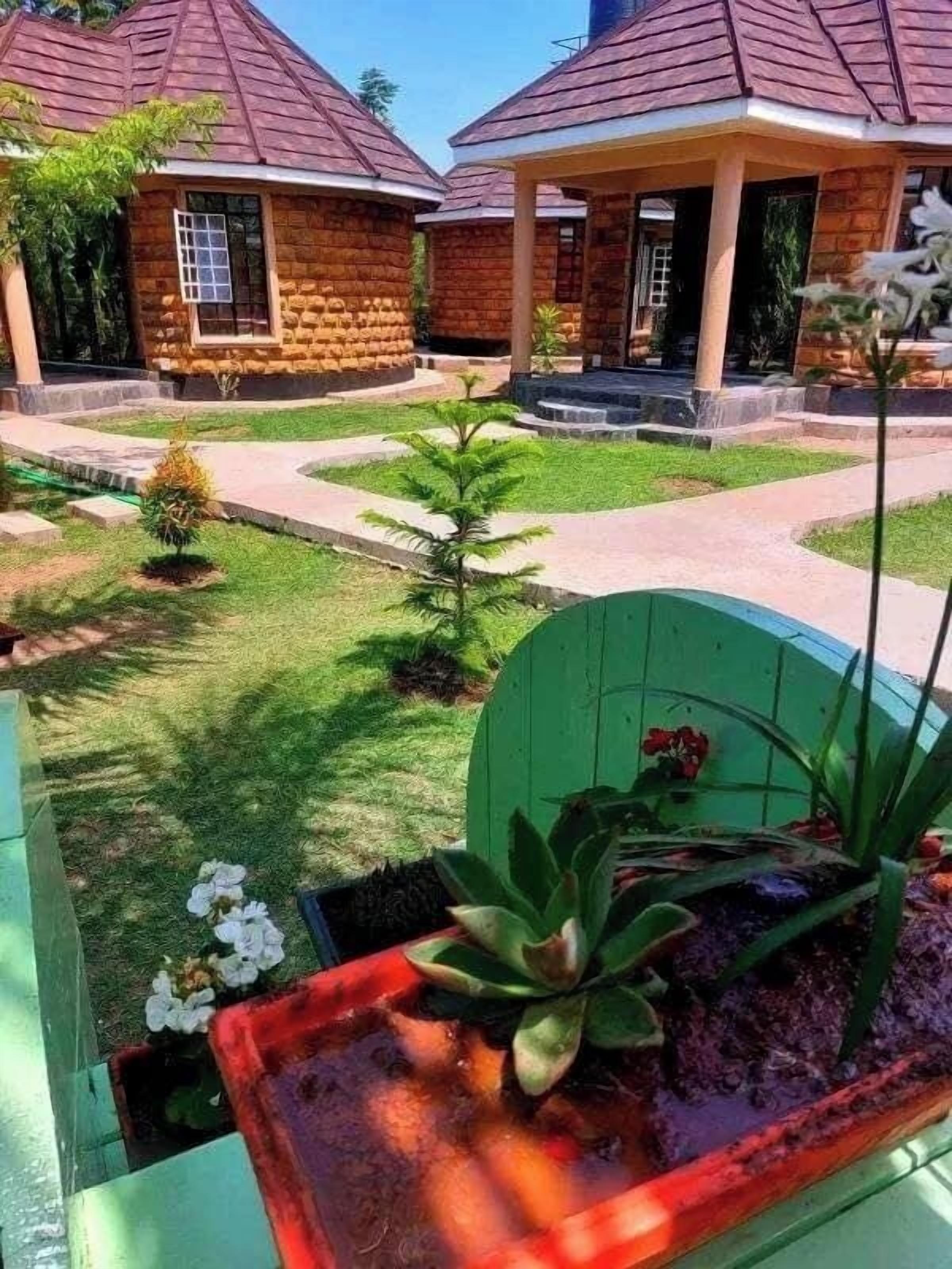 A courtyard with stone buildings, a green gate, and a small garden with plants and flowers.