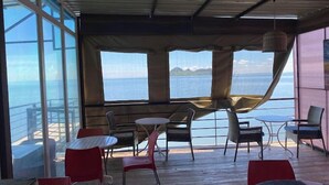 An outdoor seating area with tables and chairs, overlooking a body of water. - Lorateng' Resort Rusinga (Rusinga Island)