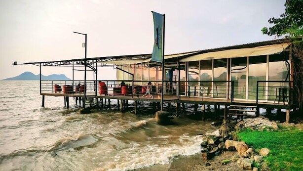 A waterfront restaurant with outdoor seating, a flag, and a view of the sea and mountains. - Lorateng' Resort Rusinga (Rusinga Island)