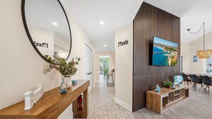 A modern hotel lobby with a wooden reception desk, a large mirror, a wall-mounted TV displaying a scenic view, and a staircase leading to another area. - The Tropical Retreat (Sarasota)