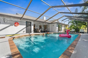 Une piscine avec une terrasse en bois, un patio couvert et un flotteur en forme de flamant rose.