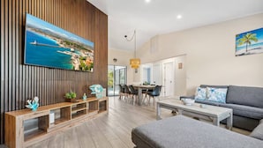 A modern living room with a large TV, wooden paneling, a dining area, and a gray sofa. - The Tropical Retreat (Sarasota)