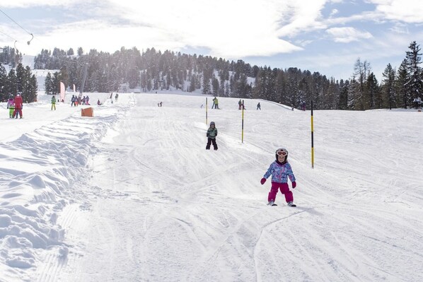 A snowy ski slope with skiers and a child in the foreground.