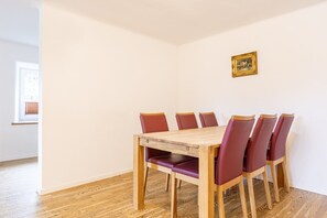 Ein Essbereich mit Holztisch und sechs Stühlen, einem Bild an der Wand und einem Fenster mit Jalousien.