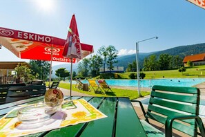 Ein Poolbereich mit Tisch, Stühlen und Sonnenschirmen.