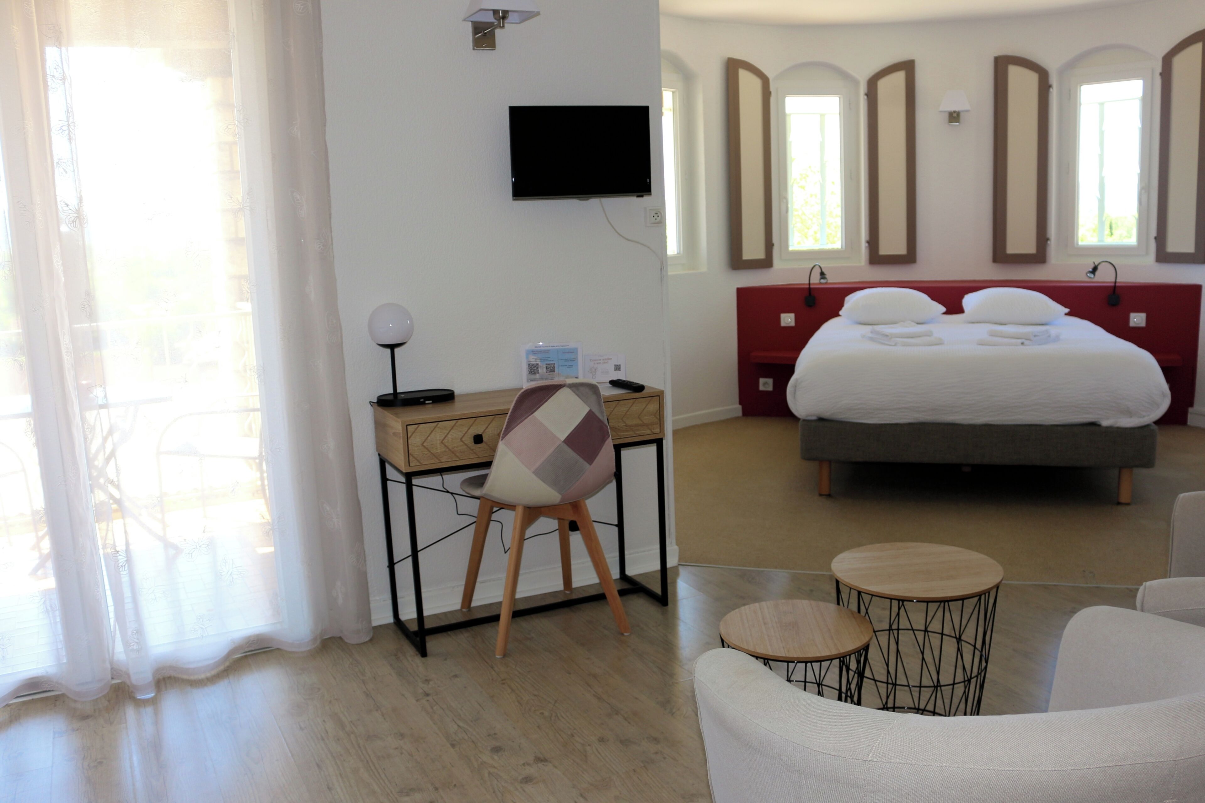 A hotel room with a bed, a desk, a chair, a TV, and a window with curtains.