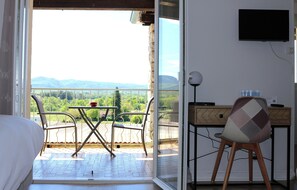 Un balcon avec une table et des chaises, un lit, un bureau avec une chaise et un téléviseur fixé au mur.