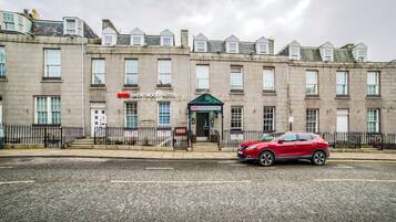 A multi-story hotel with a traditional facade, a red car parked in front, and a clear sky.