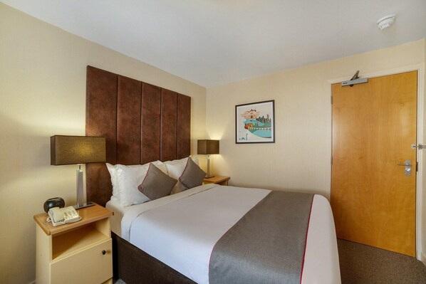 Een hotelkamer met een bed, nachtkastjes, een lamp, een telefoon en een deur.