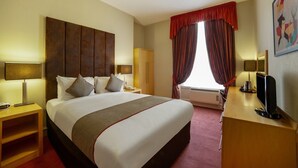 Habitación de hotel con una cama grande, un escritorio con computadora, un armario y una ventana con cortinas.